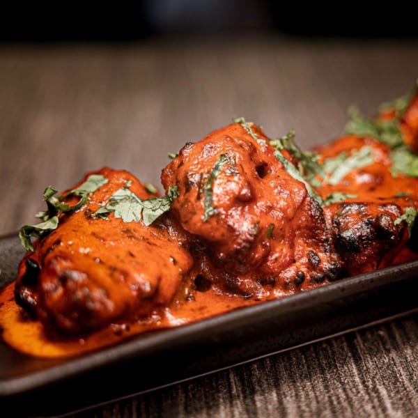 Close-up of vibrant red Indian chicken tikka pieces garnished with fresh green herbs on a dark plate.