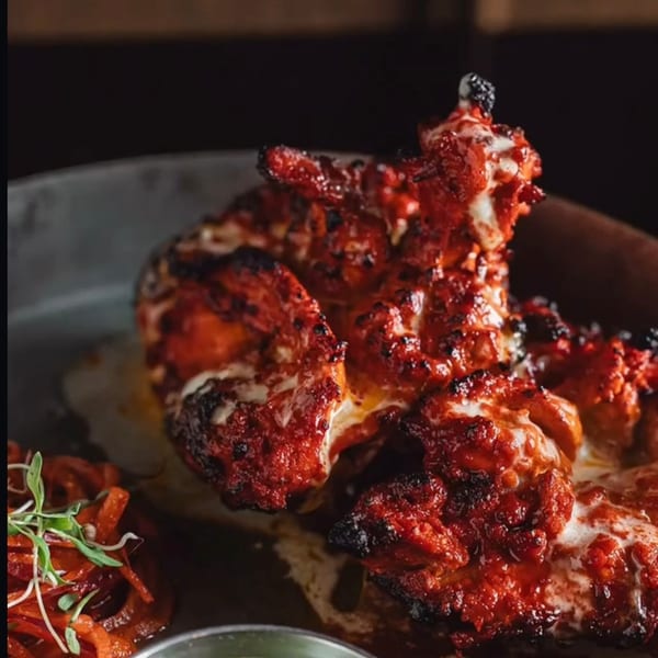 Close-up of vibrant red Indian tandoori chicken with white sauce, garnished with microgreens.