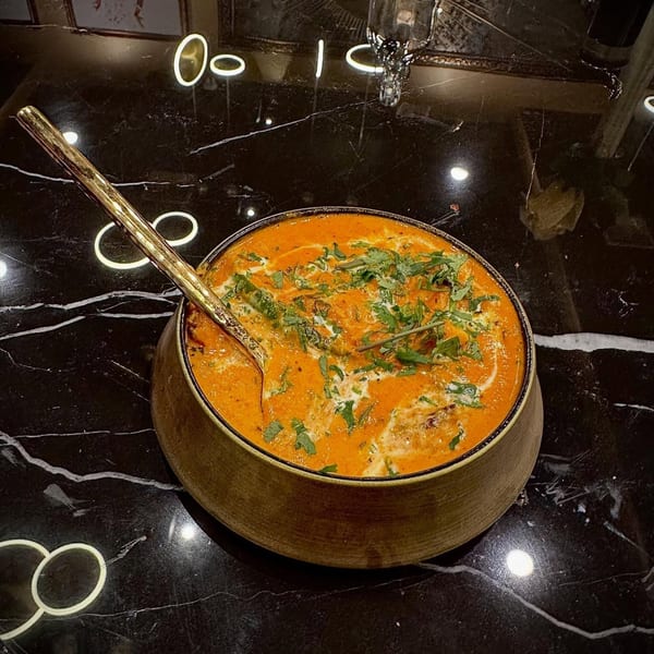Agnii's Indian curry, garnished with cream and cilantro, in a rustic bowl on a black marble table.