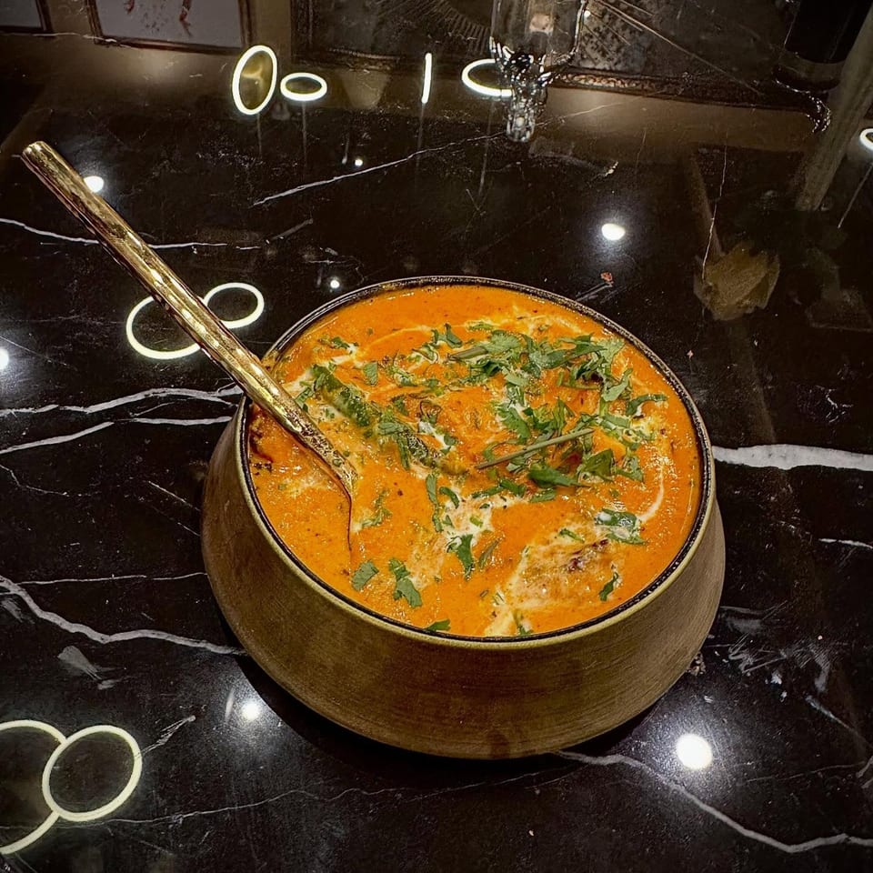 Agnii's Indian curry, garnished with cream and cilantro, in a rustic bowl on a black marble table.