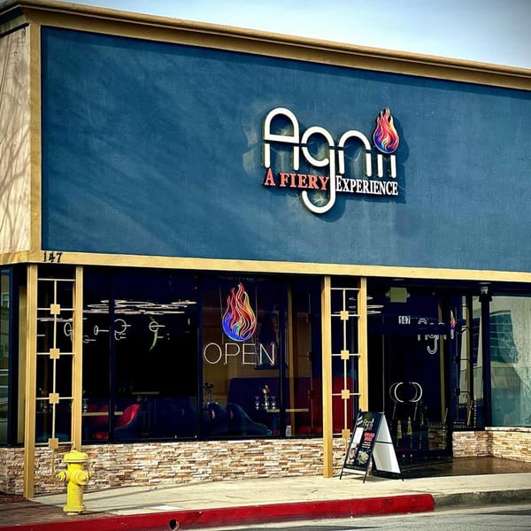 Exterior of Agnii Indian restaurant with a blue facade, gold trim, and an "OPEN" sign in the window.