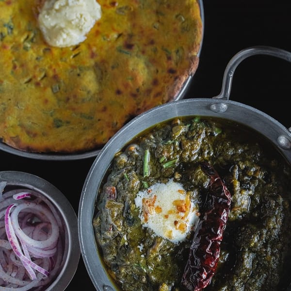 Overhead view of Indian saag, paratha with butter, and sliced red onions on a dark surface.