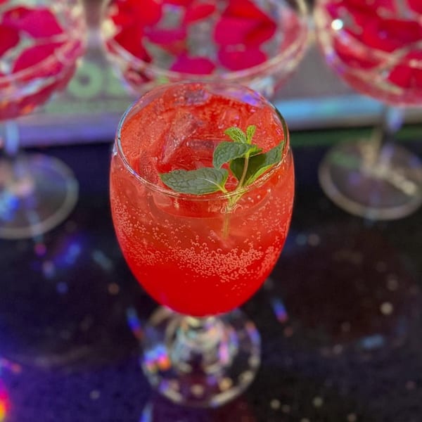 A vibrant red cocktail with ice and a mint garnish, with other drinks in the background.