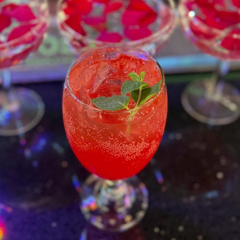 A vibrant red cocktail with ice and a mint garnish, with other drinks in the background.