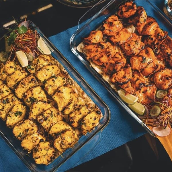 Two glass dishes of Indian chicken tikka, one yellow and one orange, garnished with lime and salad.