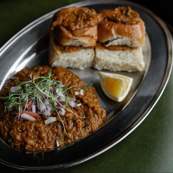 Agnii's Indian Pav Bhaji, a vegetable curry with bread rolls, garnished with onions and sprouts.