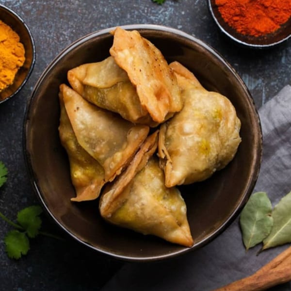 A bowl of golden-brown Indian samosas, with spices and herbs in the background.