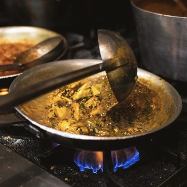 Indian curry with chicken and spices cooking in a pan over a blue flame on a stove.