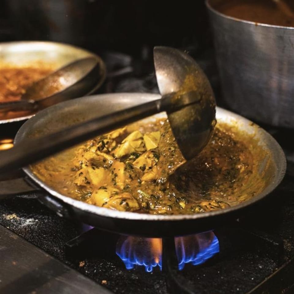Indian curry with chicken and spices cooking in a pan over a blue flame on a stove.