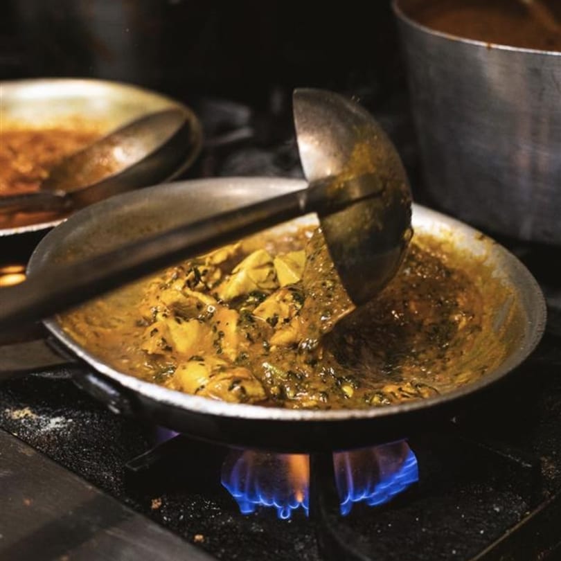 Indian curry with chicken and spices cooking in a pan over a blue flame on a stove.