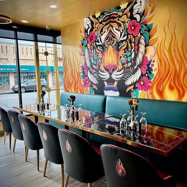 Agnii restaurant interior with a vibrant tiger mural, teal banquettes, and black chairs with flame logos.