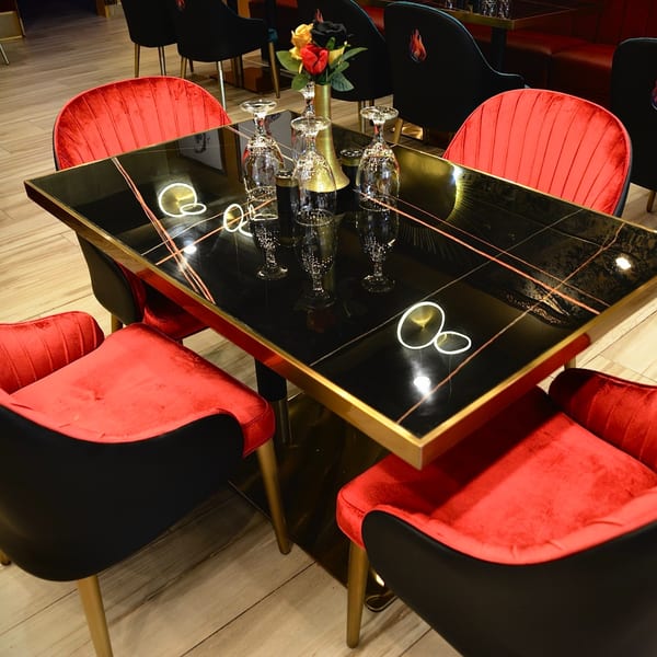 Agnii restaurant table with black marble top, gold trim, wine glasses, and red velvet chairs.