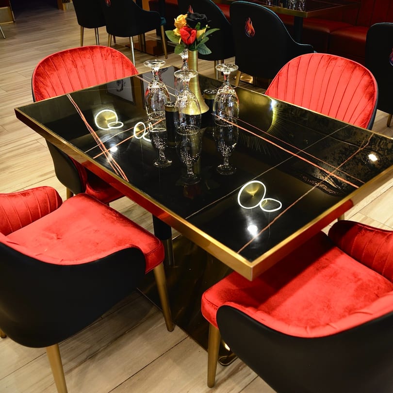 Agnii restaurant table with black marble top, gold trim, wine glasses, and red velvet chairs.