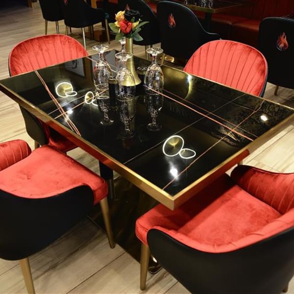 Elegant dining table with black marble top, gold trim, red velvet chairs, and wine glasses.