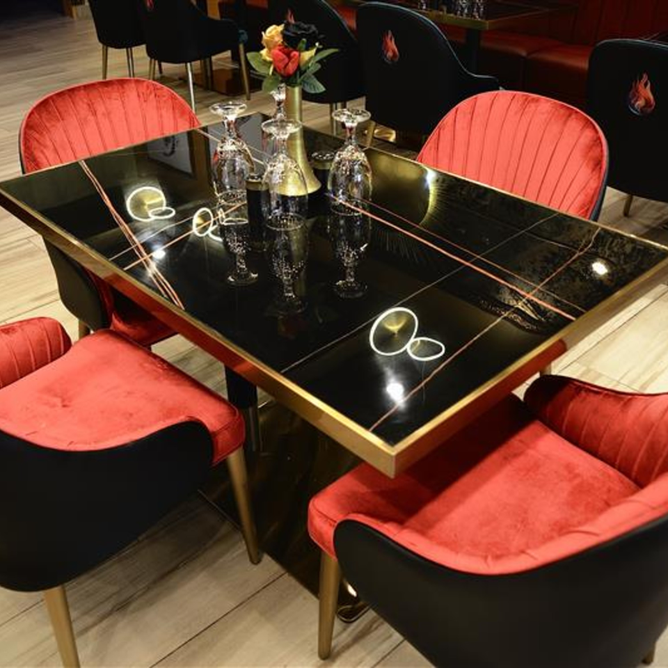 Elegant dining table with black marble top, gold trim, red velvet chairs, and wine glasses.