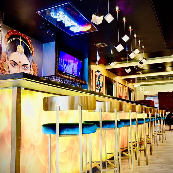 Agnii's bar area with a fiery-patterned counter, blue velvet stools, and Indian-themed decor.