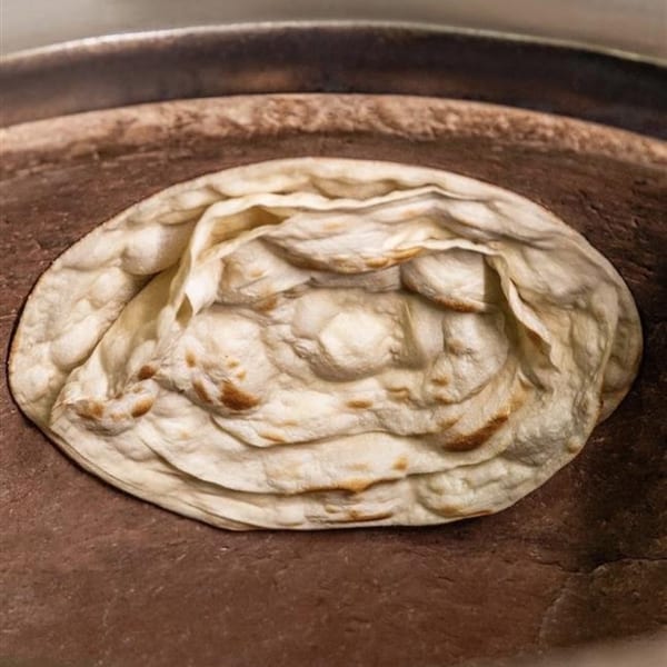 Indian naan bread baking inside a traditional tandoor oven, showing golden-brown spots.