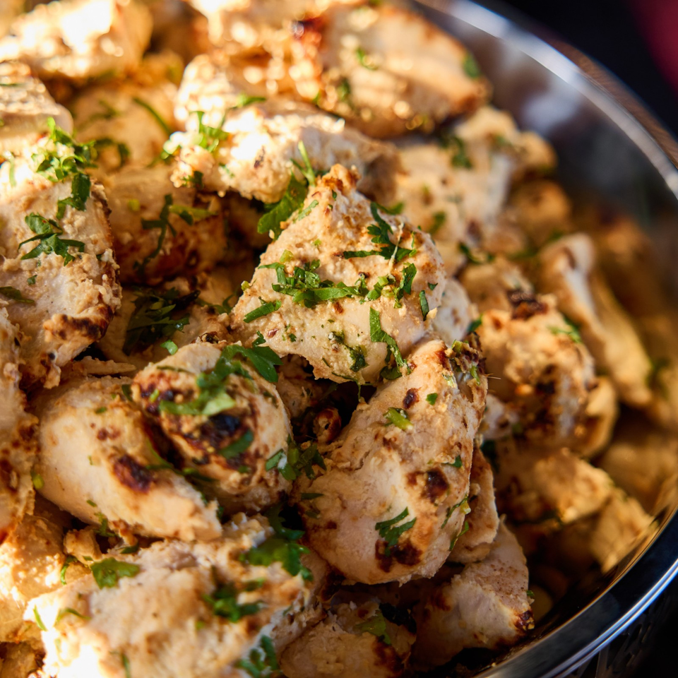 Grilled chicken pieces garnished with fresh parsley, piled on a serving platter.
